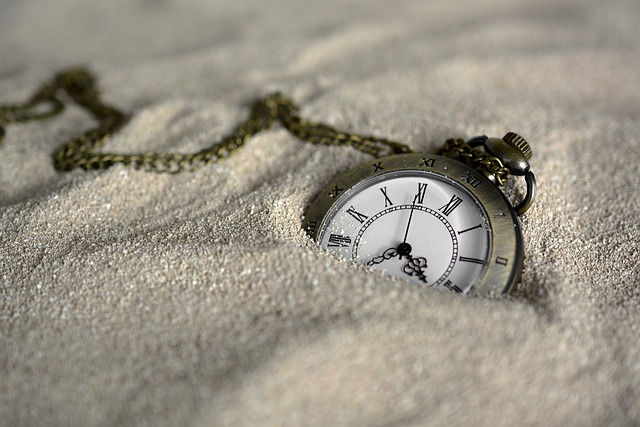 Eine alte Taschenuhr liegt halb vergraben im Sand.